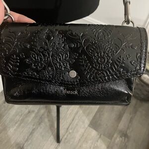 The Sak black small crossbody bag with embossed floral design and woven strap.